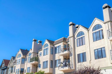 San Francisco houses in California with balconies against the sky. Row of houses facade with painted white exterior casement and arched windows.