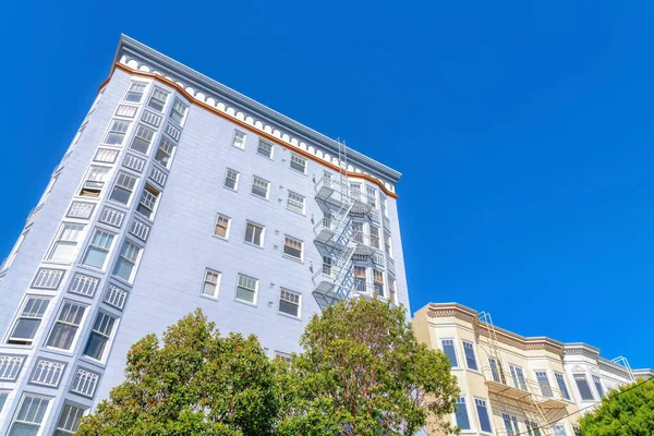 Mid-rise and low rise apartment buildings with emergency stairs at San Francisco, California. There is a blue mid-rise building on the left near the low-rise beige buildings on the right.