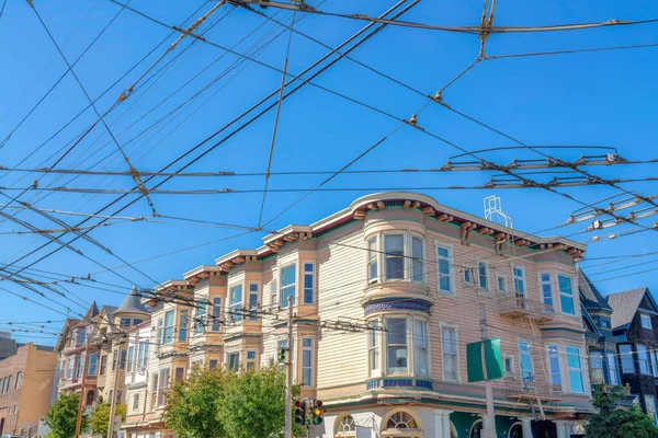Cable car trolley electric wires at the front of residential buildings at San Francisco, CA. There are intersecting wires above at the front of apartment buildings near the traffic lights.