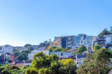 Large residential buildings on a slope at San Francisco, California. There are trees at the front and a view of multi-storey residential buildings with balconies against the clear blue sky.
