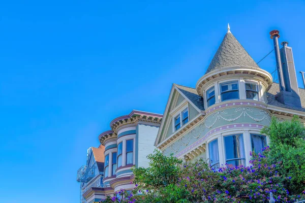 San Francisco victorian houses in a low angle view against the sky. There is a house at the front with turret wall and flues beside the house with decorative dentils.
