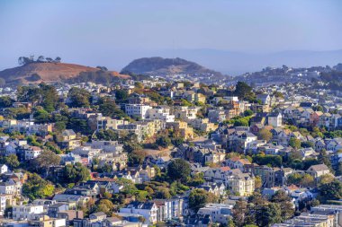 Row of residential buildings on a sloped suburbs of San Francisco, California. There are views of townhouses and apartment buildings near the mountains at the background.
