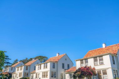 Mediterranean style cottages in San Francisco, California. Two-storey homes with clay tile roofs and paned windows against the clear sky background.