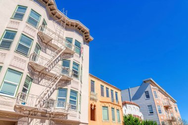 Facade of residential buildings with decorative exterior in San Francisco, CA. There is a building on the left with emergency stairs outside near the bay windows beside the mediterranean houses.