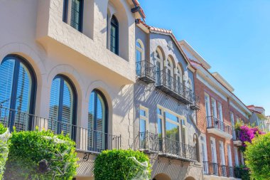 Row of houses with european style exterior in San Francisco, California. There are two houses from the left with painted stucco walls and window railings beside the house on the right with bricks.