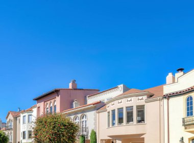 Adjacent homes with flowering trees at the front at San Francisco, California. Facade of mediterranean houses with decorative exterior against the blue sky.