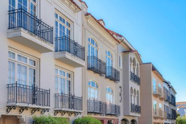 Row of mediterranean houses with wrought iron railings on its window balconies in San Francisco, CA. Facade side view of a residential buildings with stucco walls and bricks.