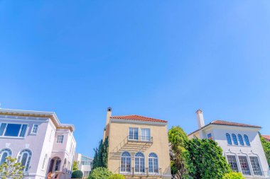 Three houses in a low angle view at San Francisco, California. There is a house on the left with victorian trims near the two houses with clay tile roofs and window railings.
