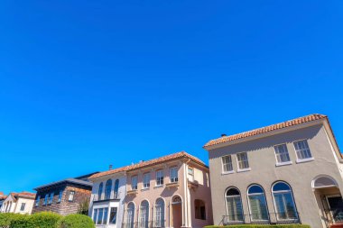 House with dark wood shingle siding along with the mediterranean houses in San Francisco, CA. Facade of houses with arched entrance and windows with railings.