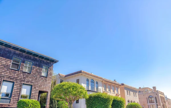 Row of mediterranean and victorian homes at San Francisco, California. There is a house on the right with dark wood shingle siding along with the mediterranean homes on the right with clay tile roofs.