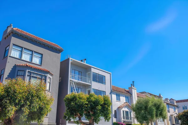 Neighborhood in San Francisco, California with modern mediterranean homes. There are trees at the front of the three-storey houses with concrete tile roofs and balconies.