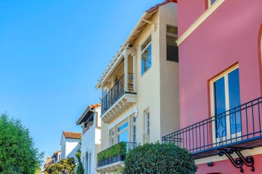 San Francisco, CA suburbs with row of painted houses with railings on windows and balconies. There is a red house on the right along with the houses with beige and white stucco walls.