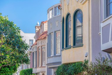 Decorative window exterior of adjacent homes at San Francisco, California. Side view of row of houses with mediterranean exterior and trees outdoors.