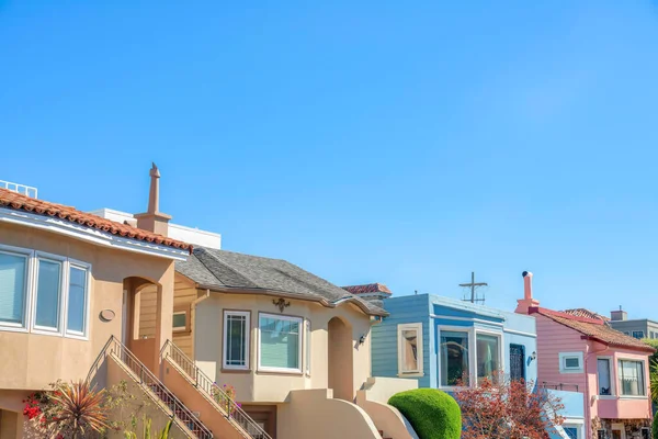 Row of houses with stairs at the entrance against the clear sky in San Francisco, CA. Colorful home entrance exterior with shrubs near the stairs leading to the front doors.