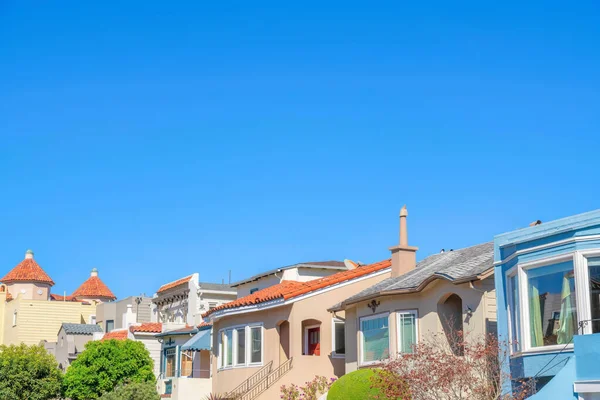 Row of houses with with clay roof tiles against the clear blue sky in San Francisco, California. Houses with staircase at the entrance leading to front doors.