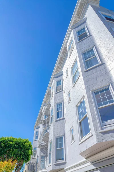 Low angle view of an apartment with white lined stucco walls and bay windows at San Francisco, CA. Low-rise apartment building with sash windows, wall vents, and emergency stairs at the front.