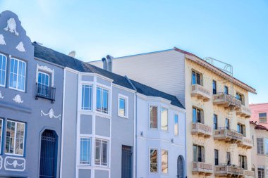 Townhomes with gray tones and a beige apartment building at San Francisco, California. There are townhouses on the left with gate at the entrance near the apartment on the right with emergency stairs.