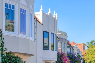 Mediterranean houses in a row with flowering plants at the front in San Francisco, CA. Row of houses with painted stucco walls and reflective glass panes.