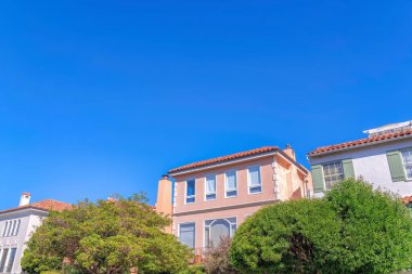 Trees at the front of residential buildings with modern mediterranean exterior at San Francisco, CA. There is a house in the middle with quoin near the house on the right with fake window shutters.