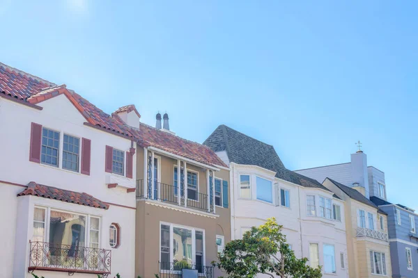 Residences in San Francisco, California against the sky. There are two houses on the left with balconies and clay tile roofs along with the houses with asphalt composite shingle roofs.