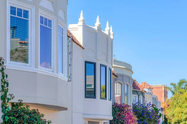 Mediterranean houses in a row with flowering plants at the front in San Francisco, CA. Row of houses with painted stucco walls and reflective glass panes.