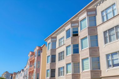 Different kinds of apartment buildings in a row at San Francisco, CA. There is an apartment on the right with stucco walls near the flat apartment building near the houses with emergency stairs.