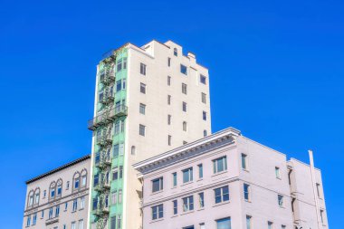 Adjacent apartment and condominium buildings at San Francisco, California. There is a high-rise building with emergency stairs and green window exterior in the middle of two mid-rise buildings.