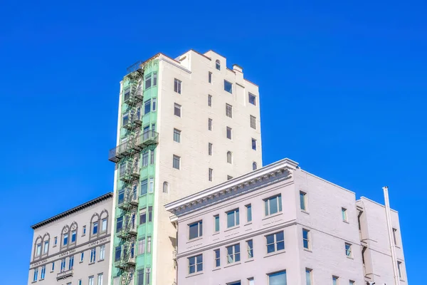 Adjacent apartment and condominium buildings at San Francisco, California. There is a high-rise building with emergency stairs and green window exterior in the middle of two mid-rise buildings.