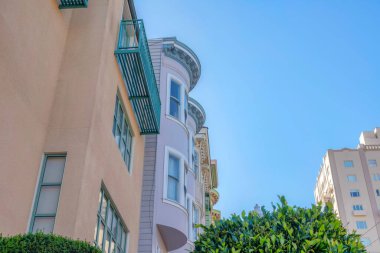 Residential buildings in San Francisco, California in a low angle view. Row of houses on the left starting with the house with balcony near the houses with curved walls and an apartment on the right.