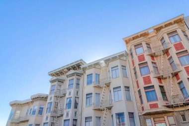 Low angle view of victorian apartment buildings with emergency stairs in San Francisco, CA. Adjacent residential buildings with bay windows against the clear sky background.