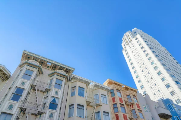 Low-rise apartment buildings beside the high-rise building in a low angle view at San Francisco, CA. There are low-rise victorian buildings on the left and a high-rise modern building on the right.