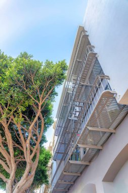 Low angle view of a low-rise modern apartment with emergency stairs at San Francisco, CA. There is a tree on the left near the building on the right with railings at the front of the windows.