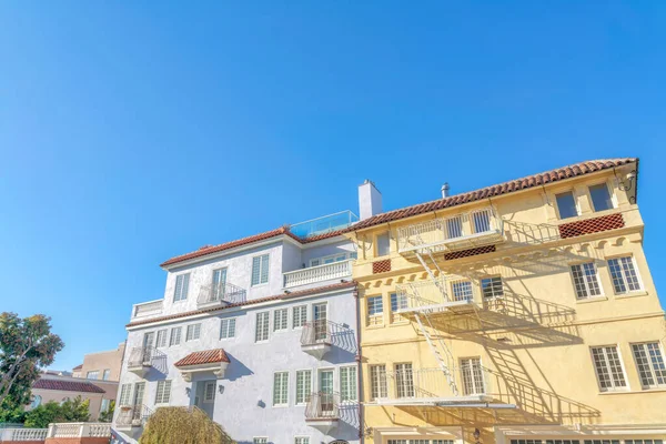 Two adjacent apartment buildings with clay roof tiles at San Francisco, CA. There is a gray building on the left with balconies beside the yellow building with emergency stairs.