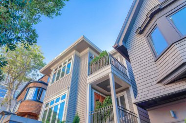 Houses with different wood shingle sidings in San Francisco, CA. There is a house on the left with curved wall and brown shingles and a house with wood lap siding near the house with gray shingles.