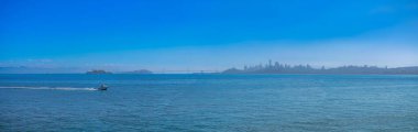 Panoramic view of San Francisco bay against the city skyline in California. There is a speed boat on the left with a view of faint cityscape at the back.