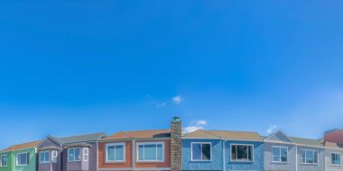 Colorful adjacent suburban houses below the clear sky at San Francisco, California. Row of houses facade with painted stucco walls and a chimney with stone veneer in the middle.