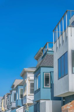 Side view of row of houses with protruding windows against the sky in San Francisco, CA. There are two houses at the front with railings on roof decks.