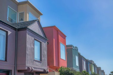 Modern small houses with painted walll exterior in San Francisco, CA. Side view of adjacent houses with picture windows at the front against the clear sky.