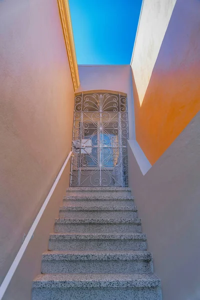 Granite stairs with wall-mounted handrails leading to a white iron single gate- San Francisco, CA. Entrance of a house in between the walls and a screened white wrought iron single gate.