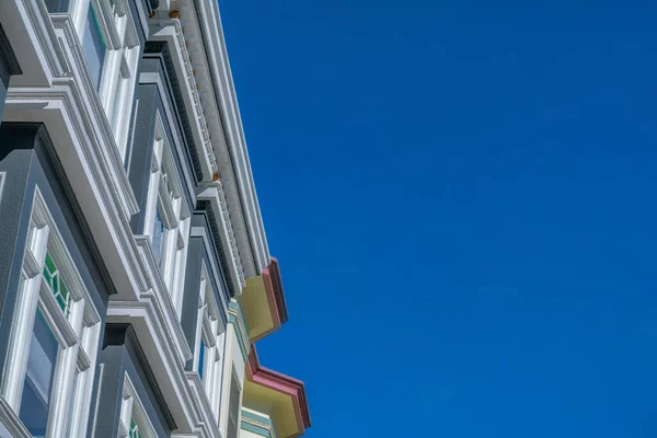 White trims of a house in a low angle view against the clear blue sky in San Francisco, CA. Home exterior with dark gray walls, paned windows, and decorative frieze board.