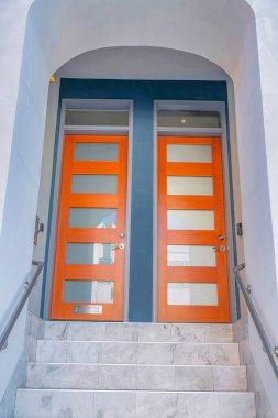 Marble stairs leading to the two front doors with glass panes and transoms in San Francisco, CA. There is a stairs at the front with marble steps and wall-mounted handrails heading to the entrance.