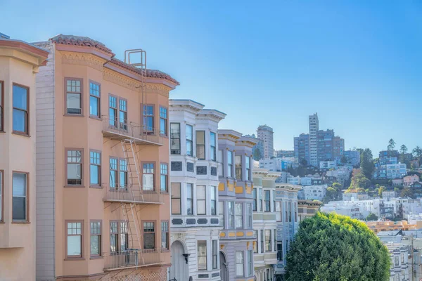 Apartment and rowhouses and view of low-rise to mid-rise buildings at the back in San Francisco, CA. There is an apartment on the left with emergency stairs beside the victorian rowhouses.