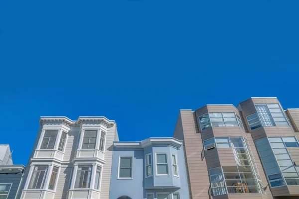 Modern and victorian style townhouses at San Francisco, CA. There is a modern house on the right with paned tall windows along with the white and light blue victorian townhouses on the left.