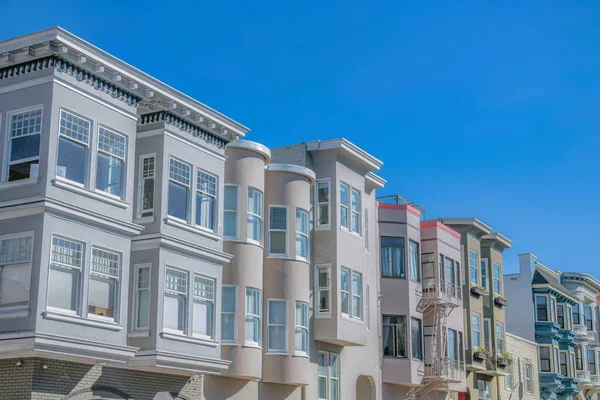 Row of large residential buildings with bay and bow windows in San Francisco, CA. There are houses with sash windows, emergency stairs, window planters, and curved window walls.