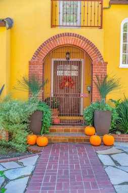Entrance of a yellow house with iron single gate and arched bricks columns- San Francisco, CA. Gate entrance with potted plants and pumpkins at the front below a balcony with railings.