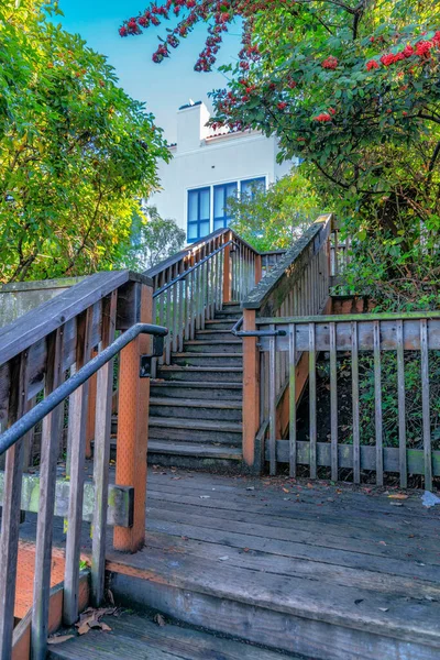Outdoor wood staircase with landing near the trees on the side- San Francisco, CA. Staircase with metal handrailings and a view of a white building at the back.