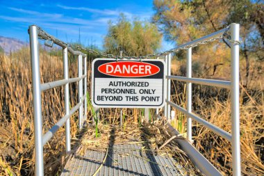 Hanging danger sign on a chainlink at Sweetwater Wetlands in Tucson, Arizona. Danger Authorized Personnel Only Beyond This Point sign on a metal deck against the dried grass at the back.