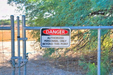 Metal wire gate with danger sign at Sweetwater Wetlands in Tucson, Arizona. Close-up of a danger signage against the dirt ground and trees at the back.