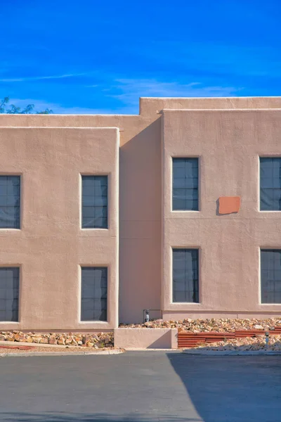 Building exterior with painted stucco wall with rocks near the wall in Tucson, Arizona. There is a concrete pavement at the front of the building with paned windows with cover and flat roof structure.