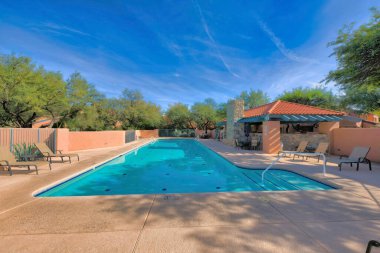 Community pool with painted peach wall and railings in a residential area at Tucson, AZ. There are lounge chairs at the side of the pool and a view of the clubhouse building on the right.